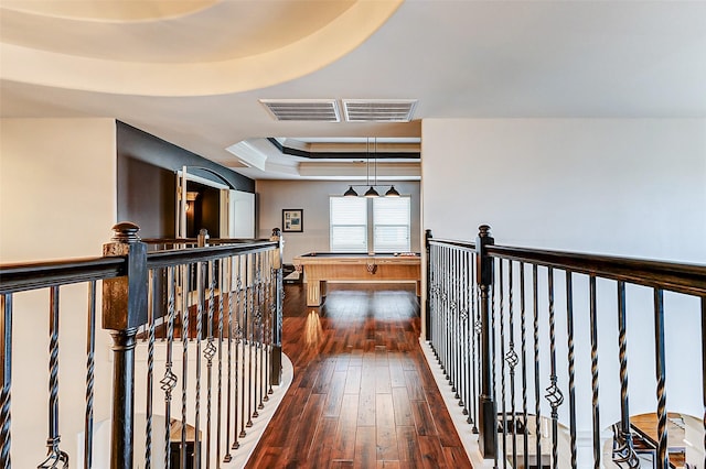 hallway featuring dark wood-type flooring, an upstairs landing, visible vents, and a tray ceiling
