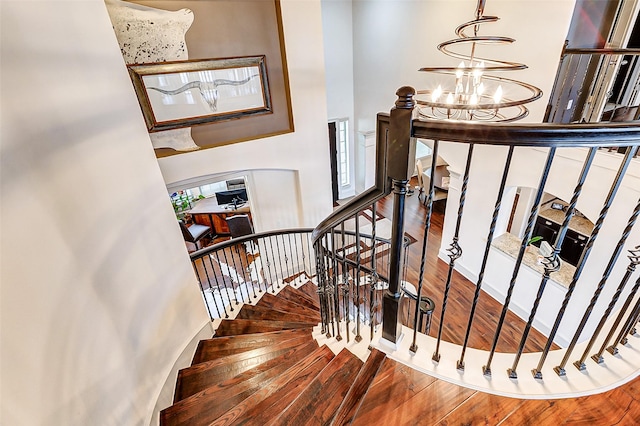 stairs with a chandelier, wood finished floors, and a towering ceiling