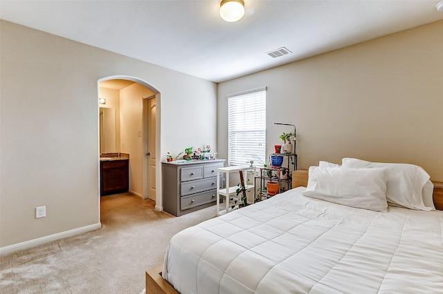 bedroom with arched walkways, baseboards, visible vents, light colored carpet, and ensuite bath