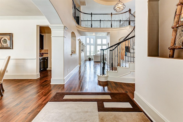 foyer entrance with arched walkways, wood finished floors, visible vents, and decorative columns