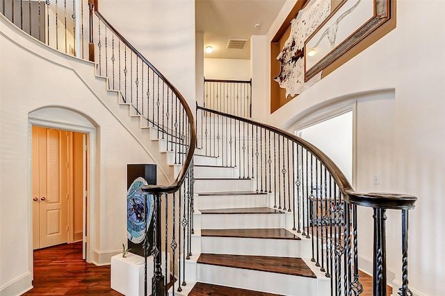 stairs featuring arched walkways, baseboards, visible vents, a towering ceiling, and wood finished floors