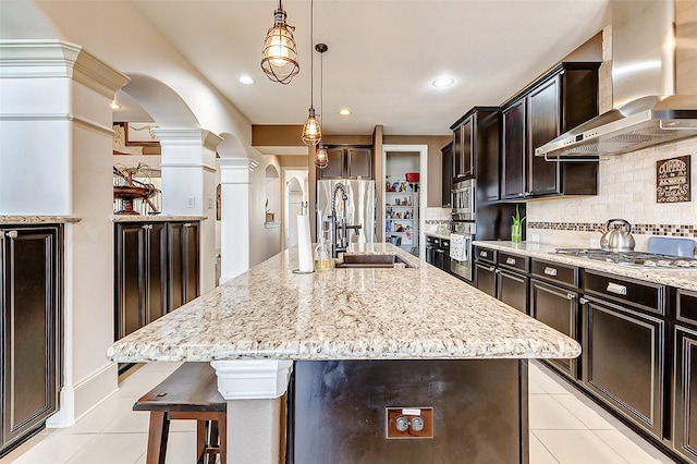 kitchen with arched walkways, wall chimney exhaust hood, light tile patterned flooring, and ornate columns