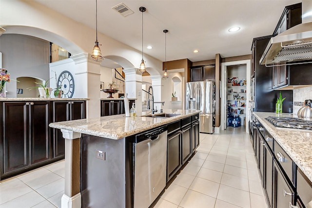 kitchen featuring stainless steel appliances, arched walkways, a sink, light tile patterned flooring, and wall chimney range hood
