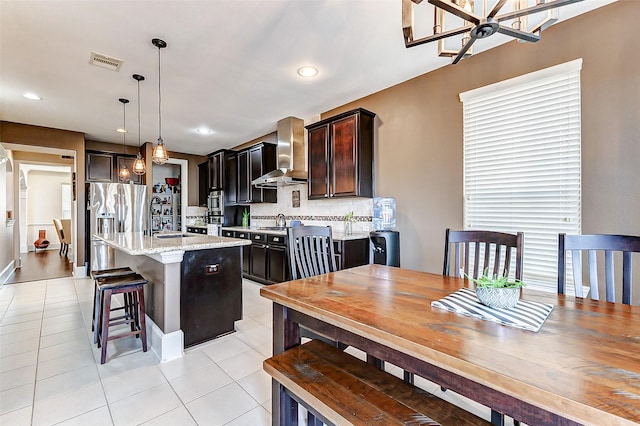 kitchen with wall chimney exhaust hood, light tile patterned flooring, visible vents, an inviting chandelier, and decorative backsplash