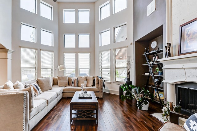 living area with a high ceiling, a fireplace, dark wood-type flooring, and a healthy amount of sunlight