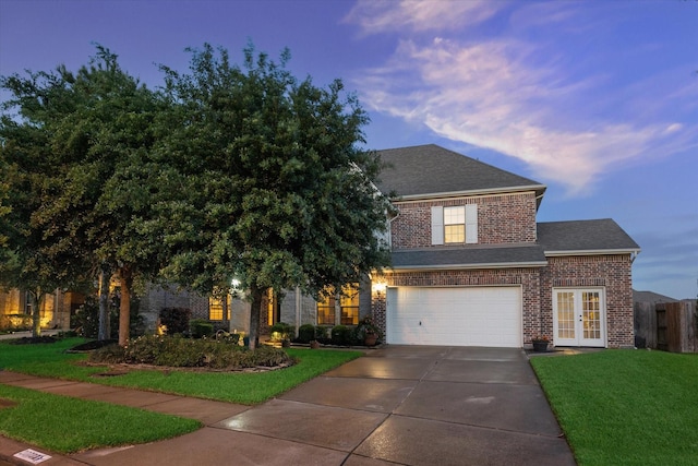 view of front of property featuring french doors, driveway, brick siding, an attached garage, and a front yard
