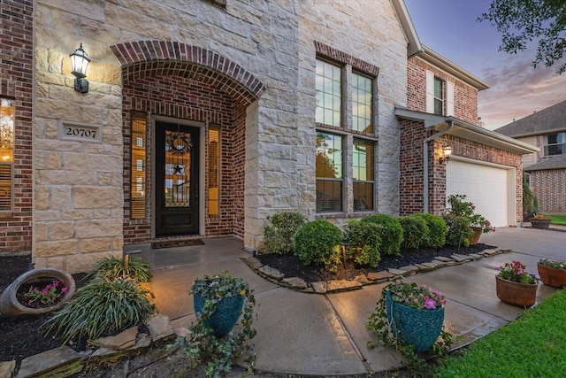 entrance to property with brick siding, driveway, stone siding, and a garage