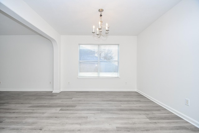 unfurnished dining area featuring arched walkways, baseboards, a notable chandelier, and wood finished floors