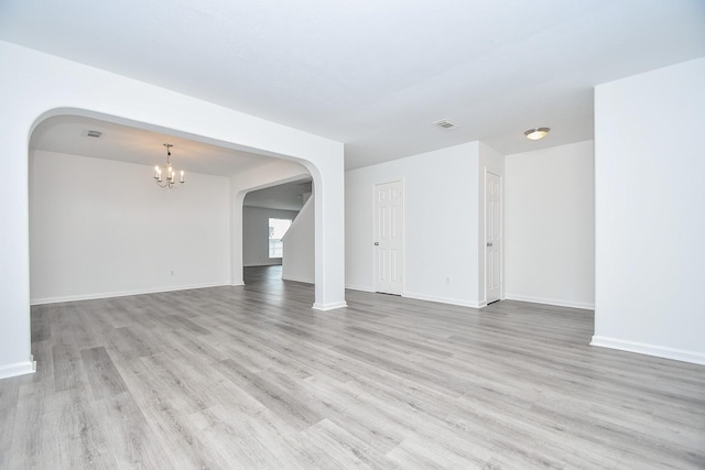 unfurnished living room featuring arched walkways, a chandelier, wood finished floors, and baseboards