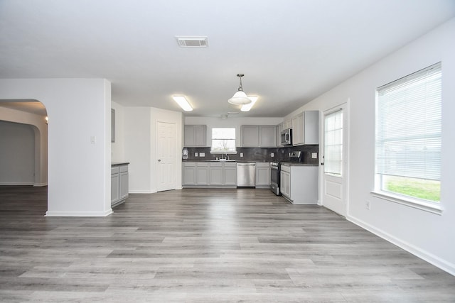 kitchen with a sink, light wood finished floors, appliances with stainless steel finishes, gray cabinetry, and visible vents