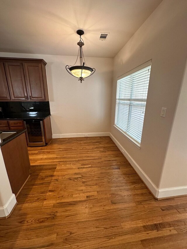 unfurnished dining area with beverage cooler, visible vents, baseboards, and wood finished floors