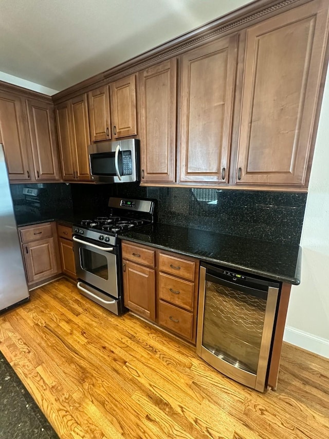 kitchen featuring light wood finished floors, stainless steel appliances, dark stone counters, tasteful backsplash, and beverage cooler