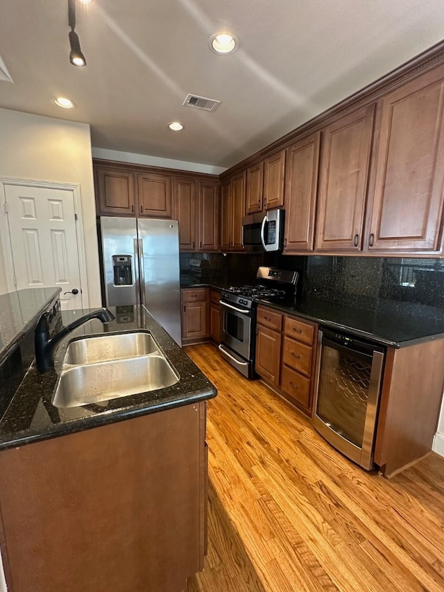 kitchen with a sink, light wood-style floors, a kitchen island with sink, stainless steel appliances, and visible vents