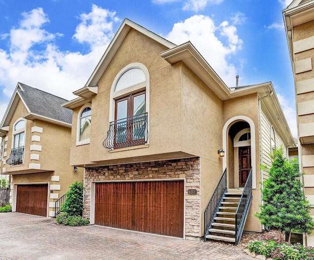 view of front facade featuring stucco siding, decorative driveway, stone siding, and a garage