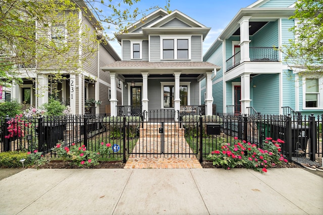 view of front facade with a porch, a fenced front yard, and a shingled roof