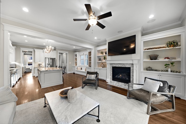 living room featuring a fireplace with flush hearth, crown molding, dark wood-style floors, and ceiling fan with notable chandelier