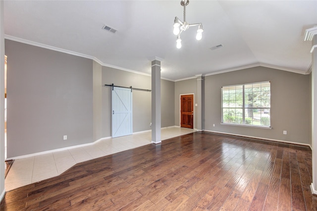 unfurnished living room with a barn door, hardwood / wood-style floors, visible vents, and decorative columns