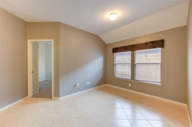 spare room featuring baseboards, lofted ceiling, and light tile patterned floors