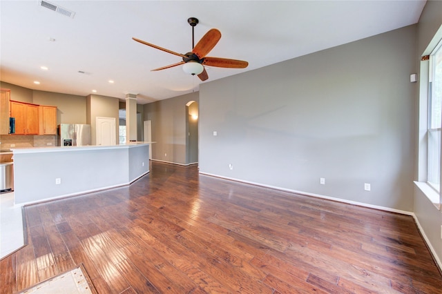unfurnished living room with dark wood-style flooring, a ceiling fan, visible vents, and a healthy amount of sunlight