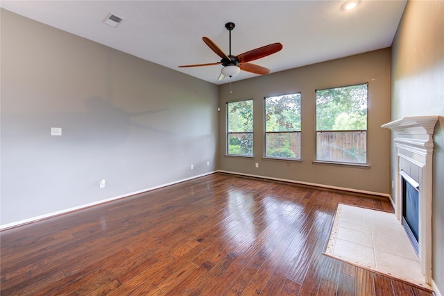 unfurnished living room with hardwood / wood-style floors, ceiling fan, a tiled fireplace, baseboards, and visible vents