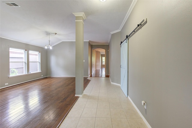 interior space featuring a barn door, arched walkways, baseboards, ornamental molding, and visible vents