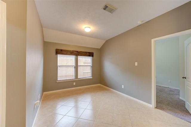 empty room with lofted ceiling, visible vents, baseboards, and light tile patterned floors