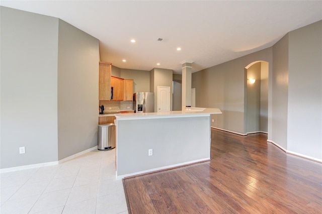 kitchen featuring stainless steel fridge with ice dispenser, light countertops, backsplash, arched walkways, and baseboards