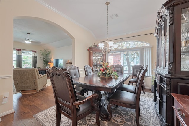 dining area with ornamental molding, wood finished floors, lofted ceiling, arched walkways, and ceiling fan with notable chandelier