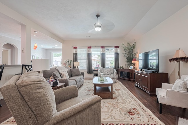 living room with a ceiling fan, arched walkways, and dark wood-type flooring