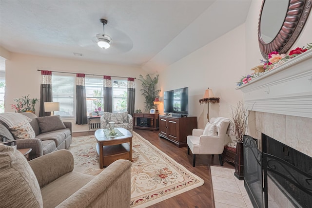 living room with a ceiling fan, a tiled fireplace, a wealth of natural light, and wood finished floors