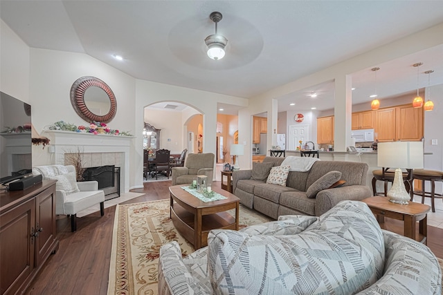 living area with ceiling fan, arched walkways, a tiled fireplace, recessed lighting, and dark wood-type flooring
