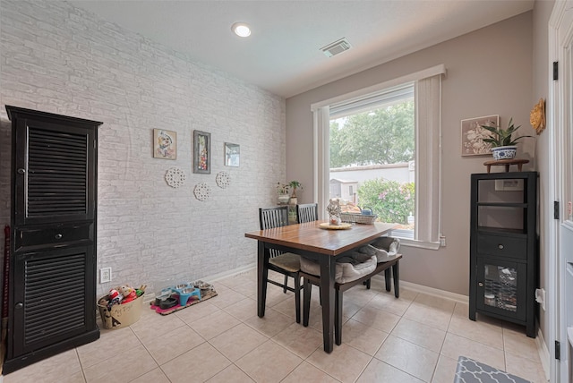 dining space with visible vents, an accent wall, brick wall, baseboards, and light tile patterned floors