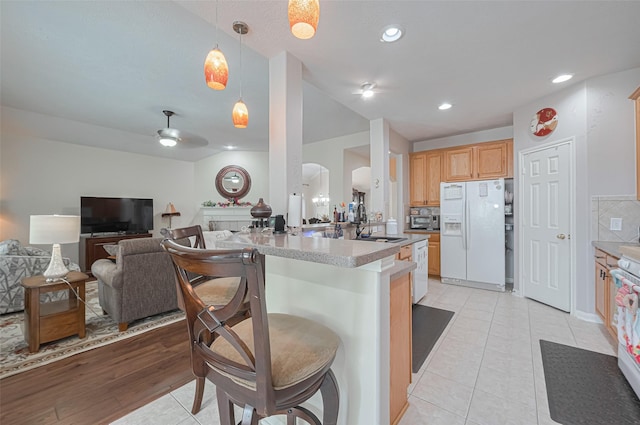 kitchen featuring a kitchen breakfast bar, light brown cabinetry, arched walkways, a sink, and white appliances