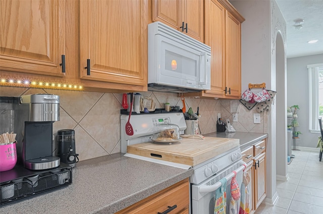 kitchen with white appliances, light countertops, arched walkways, backsplash, and light tile patterned floors