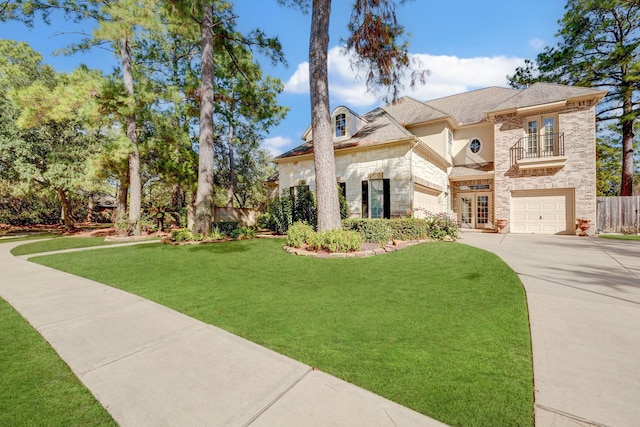 french country style house with french doors, driveway, stone siding, a balcony, and a front yard