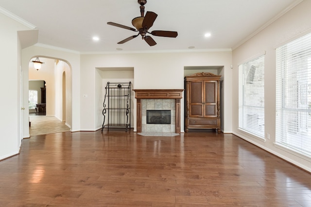 unfurnished living room featuring plenty of natural light, wood finished floors, arched walkways, and ornamental molding