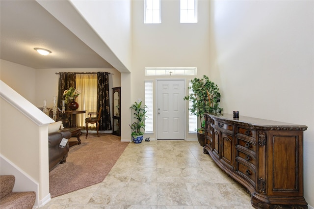 foyer entrance with baseboards, light carpet, a towering ceiling, and stairway