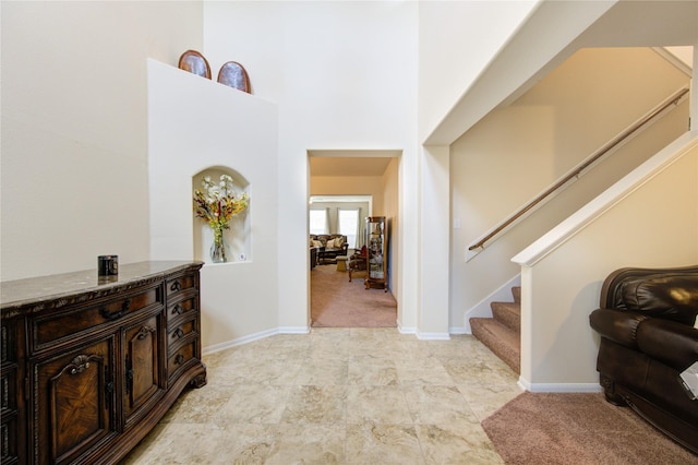 foyer featuring baseboards, a high ceiling, stairway, and light colored carpet