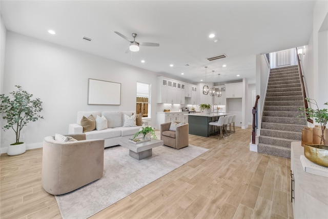 living room with light wood finished floors, a ceiling fan, recessed lighting, and stairs