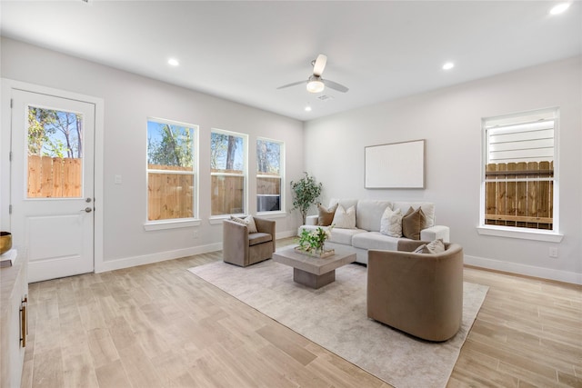 living area featuring light wood finished floors, a ceiling fan, baseboards, and a healthy amount of sunlight