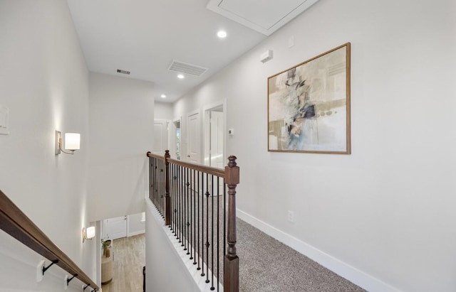 hall with attic access, visible vents, baseboards, and an upstairs landing