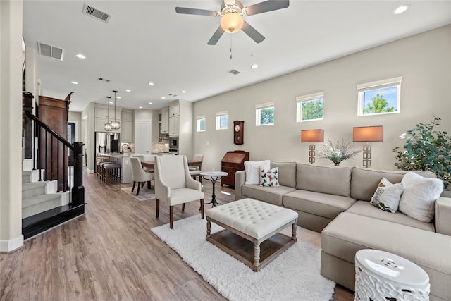 living area with stairs, a ceiling fan, visible vents, and light wood-style floors