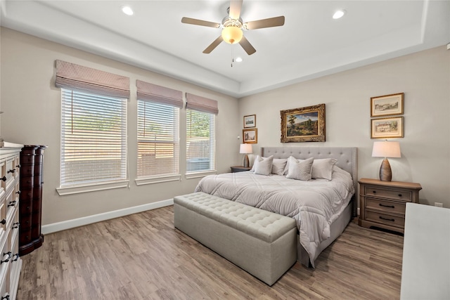 bedroom with a ceiling fan, baseboards, light wood finished floors, a tray ceiling, and recessed lighting
