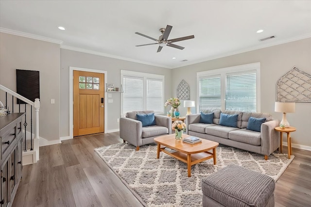 living room with wood finished floors, visible vents, a ceiling fan, crown molding, and baseboards