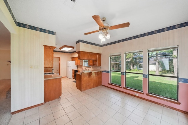 12 Cherry Hill Dr, Conroe, TX 77304 - kitchen with wallpapered walls, freestanding refrigerator, a peninsula, brown cabinets, and a ceiling fan