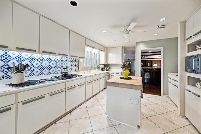 kitchen with a sink, stainless steel appliances, a ceiling fan, visible vents, and backsplash
