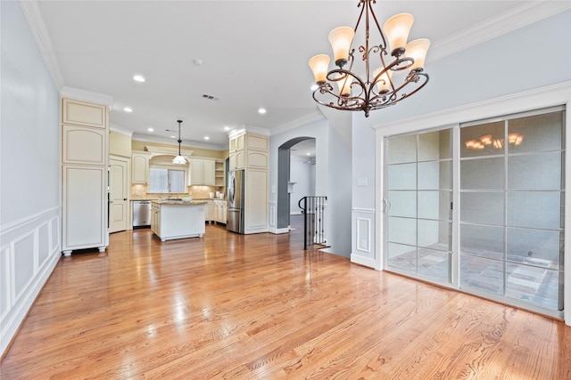 unfurnished living room featuring light wood-style flooring, arched walkways, crown molding, an inviting chandelier, and a decorative wall