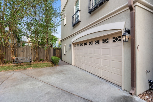 view of side of home featuring stucco siding, fence, driveway, and a garage