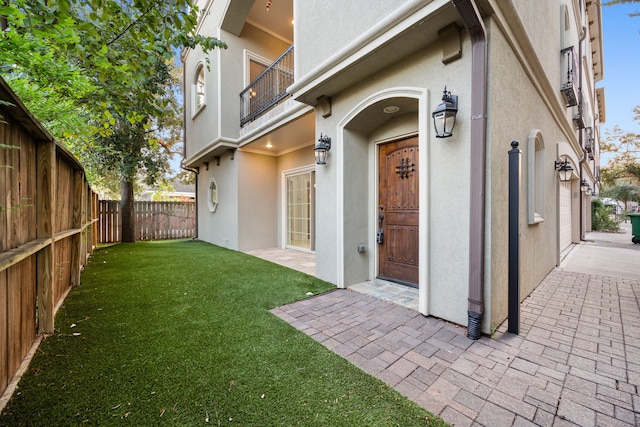 rear view of property with stucco siding, a yard, a fenced backyard, and a balcony