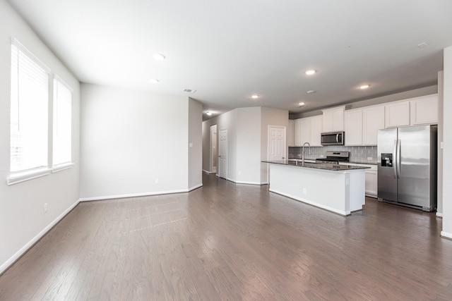 kitchen with an island with sink, stainless steel appliances, dark countertops, dark wood-type flooring, and white cabinetry